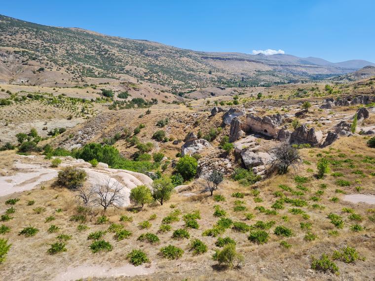 Höyüğün yer aldığı geniş arazi ve arkadaki dağ silsilesi